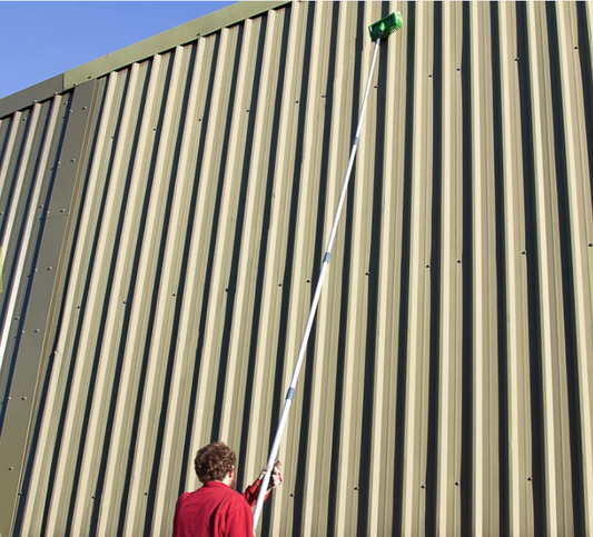 A person using a telescopic broom handle to clean a wall.